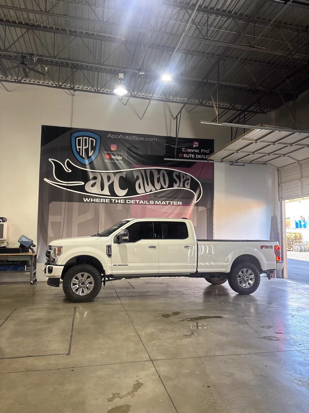 A white Ford F-350 pickup parked inside the APC Auto Spa shop in front of an APC banner