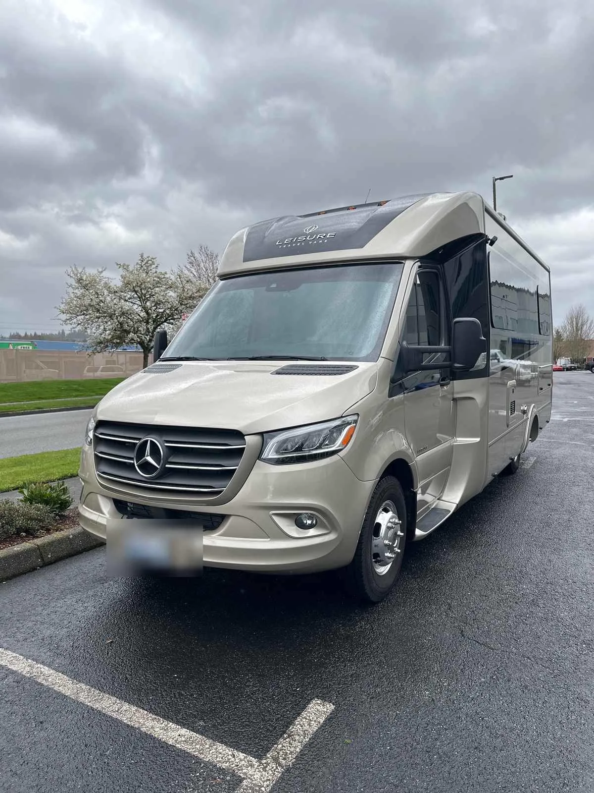 A champagne Leisure Travel Vans Class B motorhome on a Mercedes Sprinter chassis in a parking lot